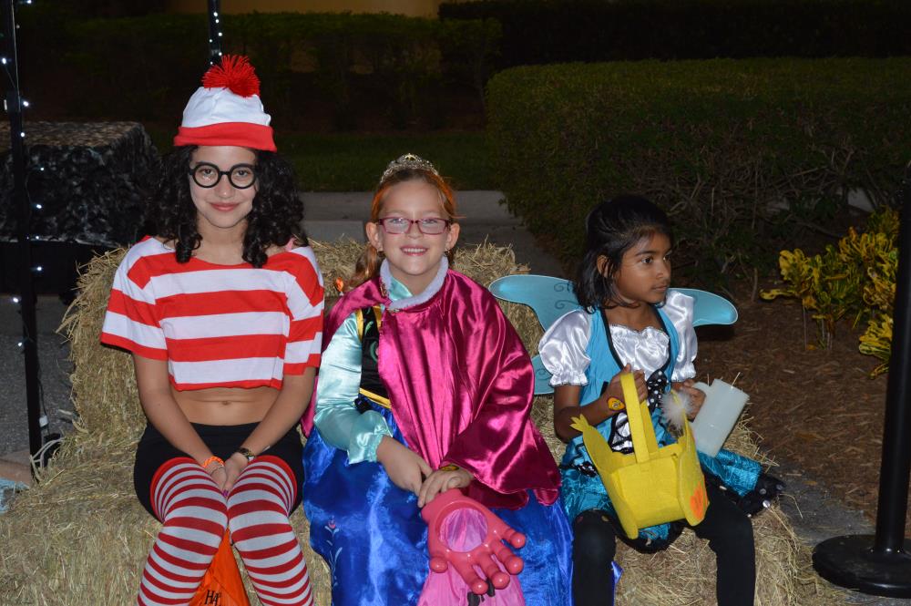 Girl in Where's Waldo costume, girl in Snow White costume and girl in blue fairy costume with yellow duck candy bag sit on hay bales
